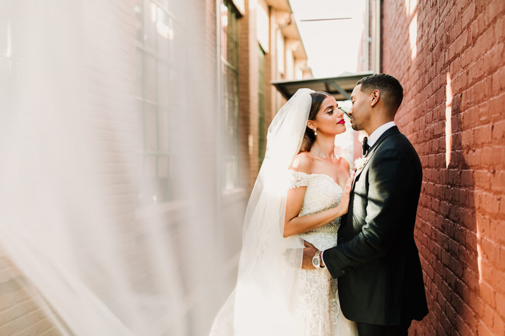 Married couple in an alley she has a big veil touching the camera lenses | Photo by Meli and Chris Atlanta Based destination Wedding Photography. 