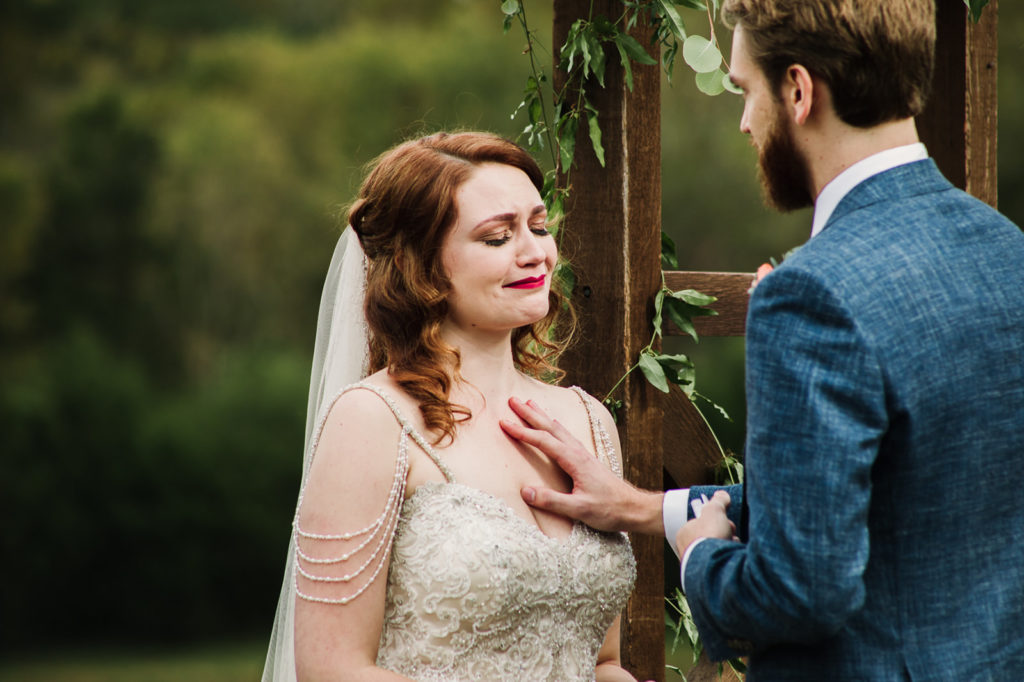 Man with blue jacket saying his vows in front of his bride with his hand on her breast in front of a wedding arch | Photo by Meli and Chris Atlanta Based destination Wedding Photography. 