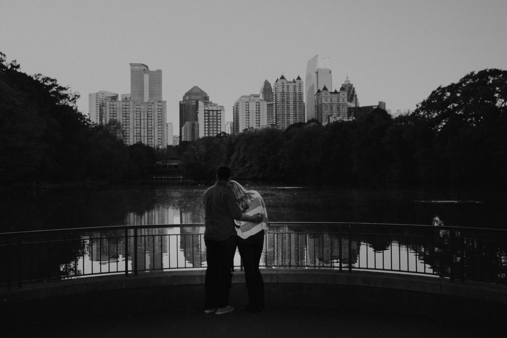 Couple hugging each other looking out at the Midtown Atlanta Georgia Skyline from Piedmont Park | Photo by Meli and Chris | Atlanta Wedding Photography