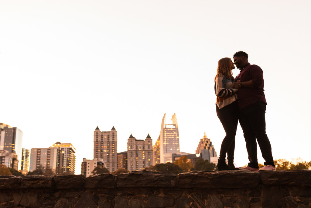 Couple hugging each other looking out at the Midtown Atlanta Georgia Skyline from Piedmont Park | Photo by Meli and Chris | Atlanta Wedding Photography