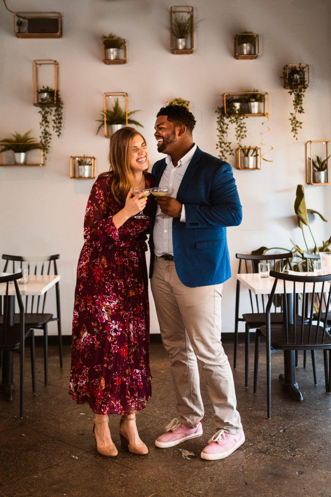 Couple side hugging and laughing holding gimlets at Whiskey Bird in Midtown Atlanta Georgia | Photo by Meli and Chris Wedding Photography