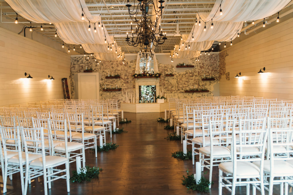 The Ceremony room inside the Cotton Gin at Mill Creek. White chair, chandelier, and white walls. Photo by Meli and Chris Wedding Photography atlweddingphotos.com