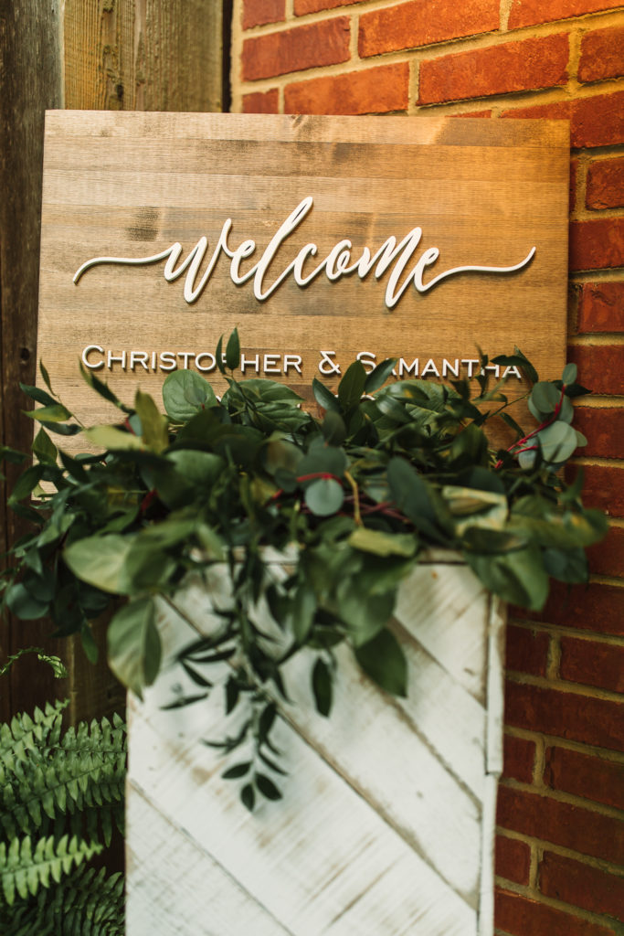 Wooden wedding Welcome sign saying "Welcome - Christopher and Samantha" in white letters. Photo by Meli and Chris Wedding Photography atlweddingphotos.com