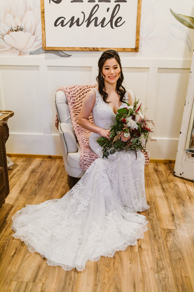 Bride sitting down wearing a long wedding dress and holding a bouquet of flowers. Inside the Cotton Gin at Mill Creek.Photo by Meli and Chris Wedding Photography.