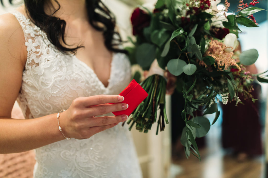 Close up of Bride holding a red envelope and green wedding bouquet inside the Cotton Gin at Mill Creek.