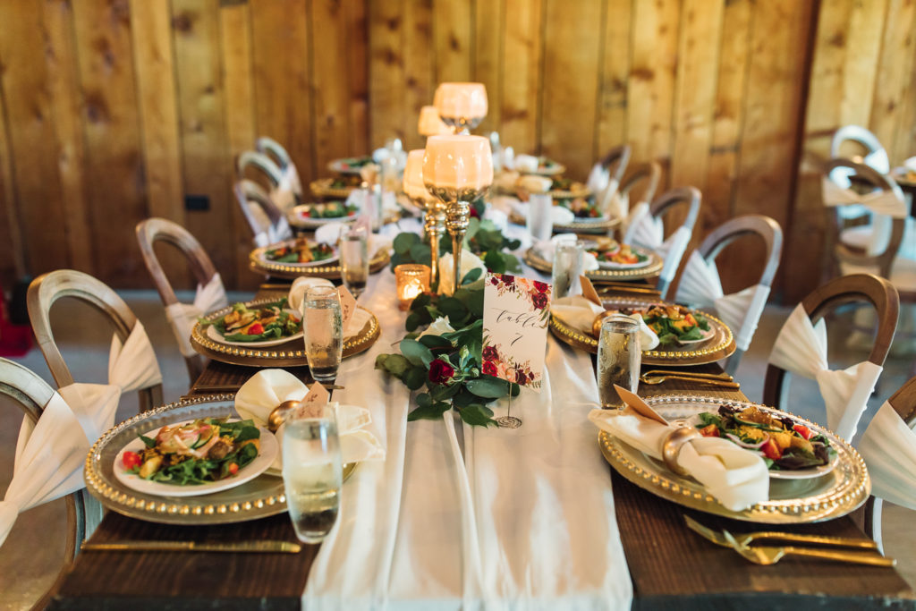 Wedding Reception table with plating, salads, candles, and champage inside the Cotton Gin at Mill Creek. Photo by Meli and Chris Wedding Photography atlweddingphotos.com