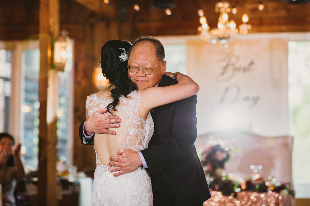 Father of the bride giving a sweet hug during the wedding reception inside the Cotton Gin at Mill Creek.. Photo by Meli and Chris Wedding Photography atlweddingphotos.com